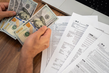 Male entrepreneur counts dollar banknotes preparing clear financial data for filling different tax forms mandatory for law-abiding taxpayers at workplace with laptopの写真素材