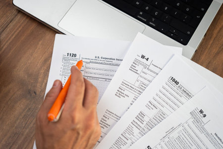 Man company accountant examines tax forms holding pen preparing for filling necessary information in compliance with federal laws sitting at workplace with laptopの写真素材