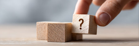 Human hand placing a wooden block with a question mark symbol on top of other plain blocks, representing problem solving, decision making, choice, and seeking answers or solutionsの素材