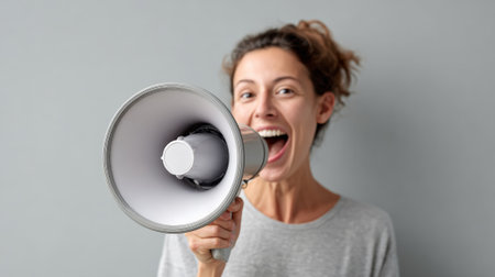Young woman holding a megaphone and shouting during a protest, expressing her dissent and fighting for social justice with passion and determinationの素材