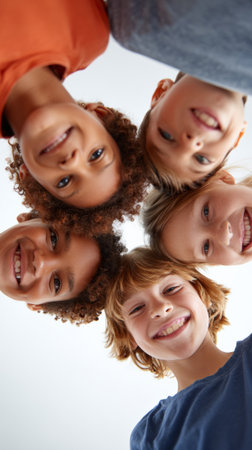 Five happy, multi ethnic children forming a circle, bending their heads down and smiling, enjoying friendship and carefree moments on a summer dayの素材
