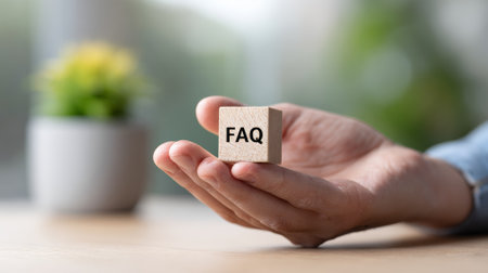 Persons hand displaying a wooden cube with faq text, symbolizing access to frequently asked questions, customer support, and helpful information for problem solvingの素材