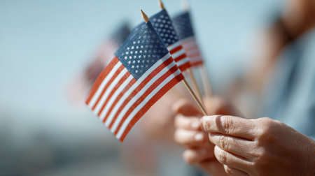 Hands waving small american flags on sticks celebrate a patriotic event, with a blurred crowd in the background embodying unity and national pride amid the festivitiesの素材