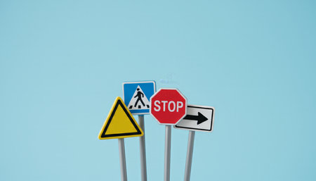 Miniature traffic signs representing a stop sign, pedestrian crossing, warning sign, and one way arrow, symbolizing the essentials of driving education and understanding road regulationsの素材