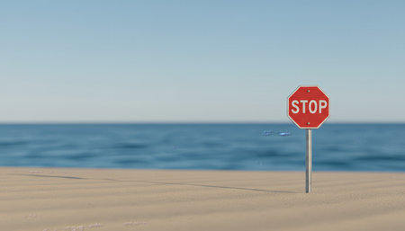 Stop sign standing on a sandy beach by the clear blue ocean, symbolizing reaching a boundary, the end of a journey, or a humorous driving lesson settingの素材