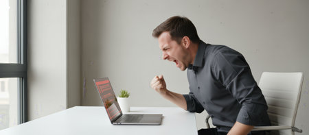 Businessman expressing anger and frustration while sitting at his desk, working on a laptop with a technical error or failing software, experiencing stress and a problemの素材