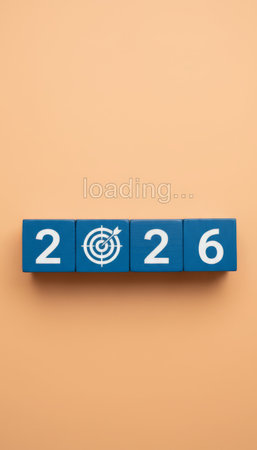 Blue wooden blocks showing 2026 with a target replacing the 0, loading... Soft peach background and emerging text suggesting new year goals, planning, ambition and forward looking progressの素材