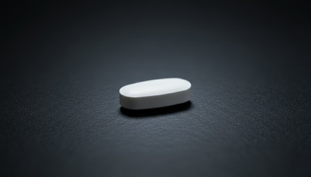 White oval tablet resting on a dark, reflective surface, creating a subtle highlight, illustrating health, medicine, treatment, and pharmaceutical productsの素材