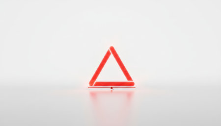 Red neon light forming a geometric triangle shape, glowing with a soft reflection on the bright white surface, symbolizing warning, danger, or attentionの素材