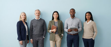 Group of multi ethnic and multi generational business people standing in a row against a light blue background, representing a diverse and inclusive workforce demonstrating professional unityの素材