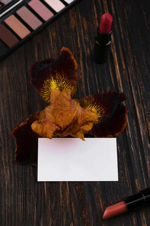 Business card, matte nude lipsticks and iris flower on a wooden table. A brown eyeshadow palette in the background. Cosmetics, trendy glamorous colorsの写真素材