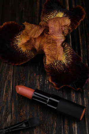 Brown matte lipstick and iris flower on a wooden table. Cosmetics, trendy glamorous colorの写真素材