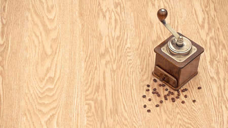 Old mechanical coffee grinder with coffee grains on a textured wooden table.の写真素材