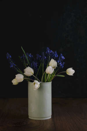 Fresh bouquet of white anemones and blue muscari flowers in a tin can on a wooden dark backgroundの写真素材