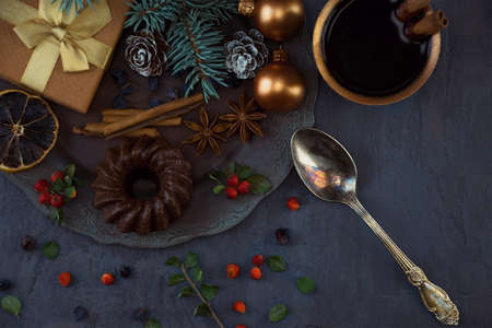 Christmas mood. Gift with toys, chocolate muffin, spices, spruce branch and berries on a metal vintage plate, silver spoon, cup of coffee with cinnamon on the table. Top viewの写真素材