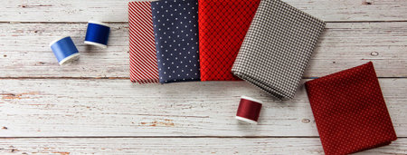 cover image. Top view to some blue and  pachwork fabrics and threads placed on light grey wooden...
