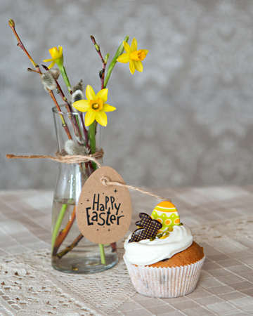 Homemade muffins on linen table cloth and daffodils flowers and willow branches bouquet in vase, light background. Spring, Easter, celebration concept. Tasty dessert. Copy space. Natural day light.の写真素材