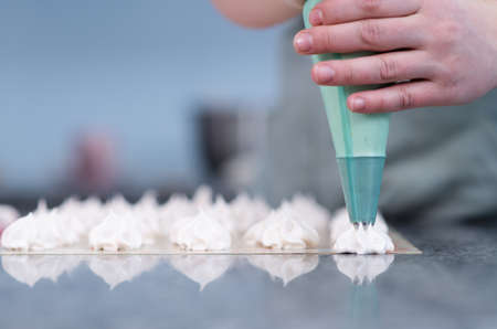 Close up hands of the chef with confectionery bag cream to parchment paper at pastry shop kitchenの写真素材