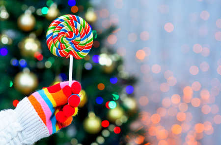 hand in multi-colored glove holds a lollipop against the background of the Christmas treeの写真素材