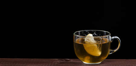 Lemon falls in a mug with tea on a black background with a lot of splashes. Frozen momentの写真素材