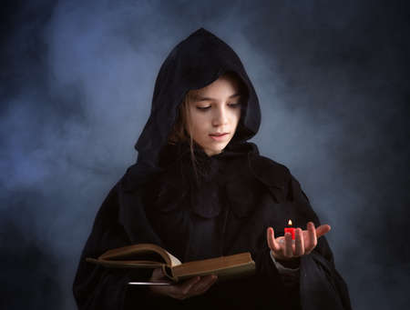 A girl in a witch's cloak with a magic wand in his hand conjures magic. Halloween outfitの写真素材