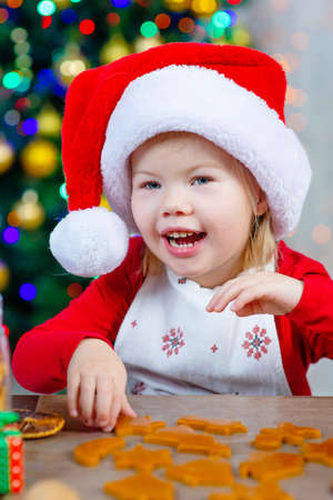 Little cute girl in santa hat bakes Christmas cookies with a smileの写真素材