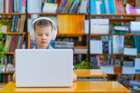 Cute boy in the library with headphones working on a laptop, focusing, looking at the screen