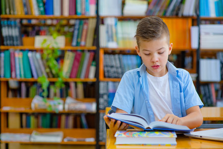 Cute boy in the library sitting at a desk and reading a book