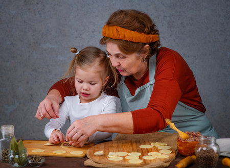 Grandmother teaches granddaughter how to make dumplings. Together they roll out the dough and mold dumplings with their handsの写真素材