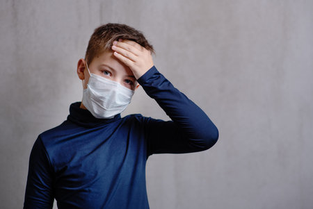 A boy in a medical mask holds his forehead with his hand. concept. stay home