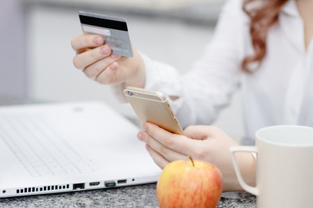 Hands holding a credit card and a phone on a background of an open laptop. Shopping Online Conceptの写真素材