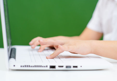 Hands are typing on a white laptop keyboard on a background of green school blackboard