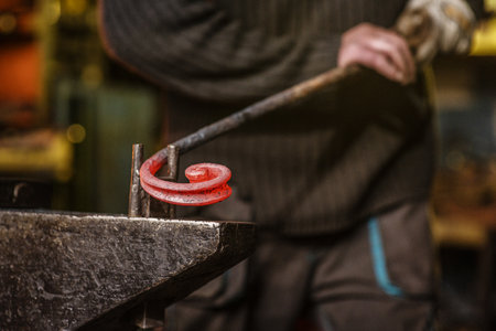 The blacksmith twists the spiral with the help of an anvil, heating the iron blank to red. Work in the forgeの写真素材