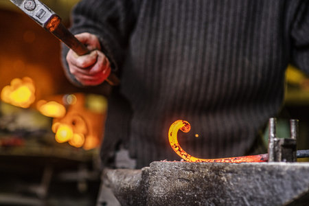 Close-up of the hands of a blacksmith twisting a spiral with a hammer, putting a red-hot iron blank...