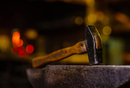 A blacksmith's hammer lying on an anvil in a dark forge. Blacksmithing tools
