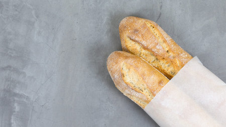 close up testy french baguettes, baked bread on grey stone table background. eco-friendly paper...