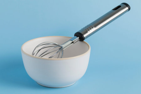 bowl and whisk on blue background. Kitchenware.