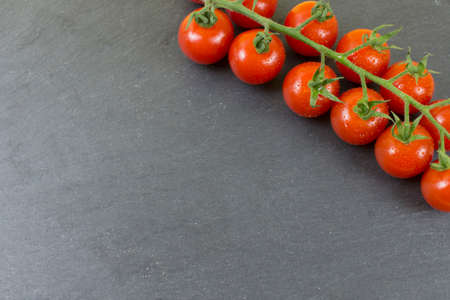 branch of small red tomatoes on black stone background.の写真素材