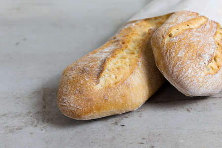 close up crusty baguettes, baked bread on grey stone table background. French bread. eco-friendly paper packaging.の写真素材