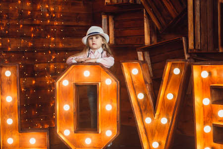 A little girl looks out from behind the wooden letters decorated with lamps and smiles.の写真素材