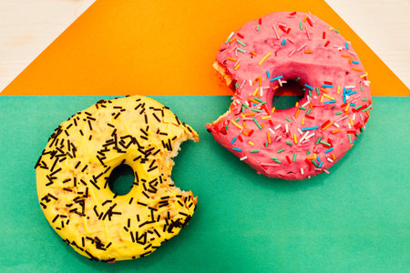 Two bright nibbled doughnuts lie on a multicolored backgroundの写真素材