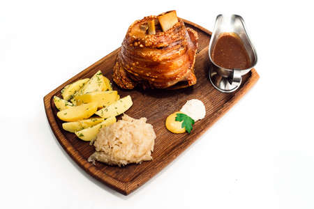 Roast pork knuckle with garnish and sauce on wooden plate. Isolated.の写真素材