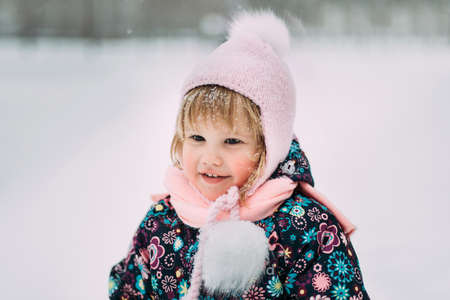Cute little girl having fun in winter park during snowfallの写真素材