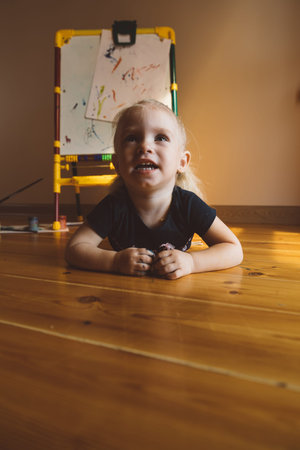 Little girl sits on the floor and draws on an easel
