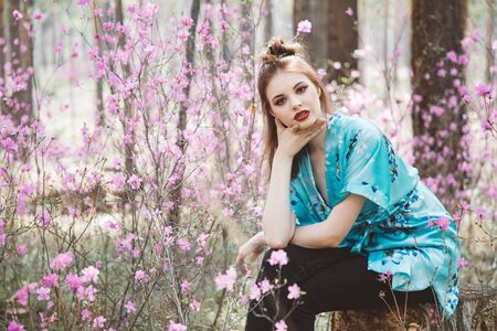 A girl dressed in Japanese style in a flowering forest among pink flowersの写真素材