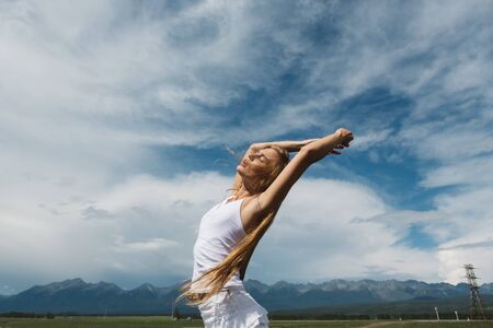 Girl in a white dress on a background of mountains and a cloudy skyの写真素材