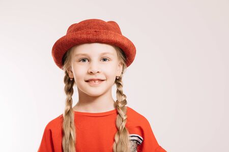 Little girl in a red suit and hat posing on a light backgroundの写真素材