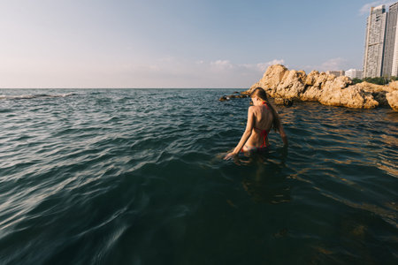 Girl with long hair swims in the sea, splashes water on a background of a sunset sky