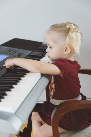 A little girl in a burgundy suit plays a synthesizer