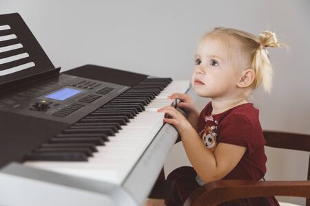 A little girl in a burgundy suit plays a synthesizerの写真素材
